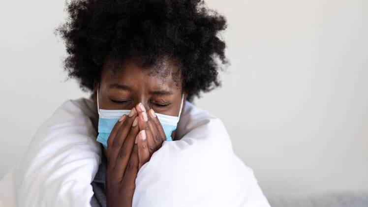 Close up of Woman with mask on, sneezing, wearing a white blanket