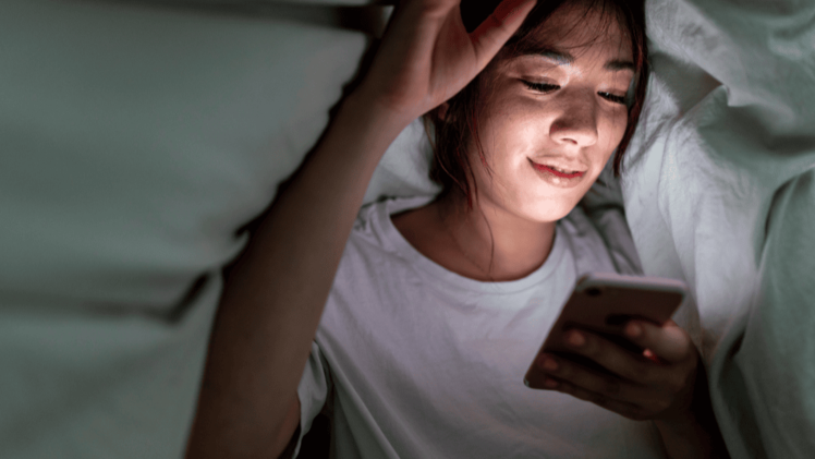 woman lying in bed scrolling on her phone