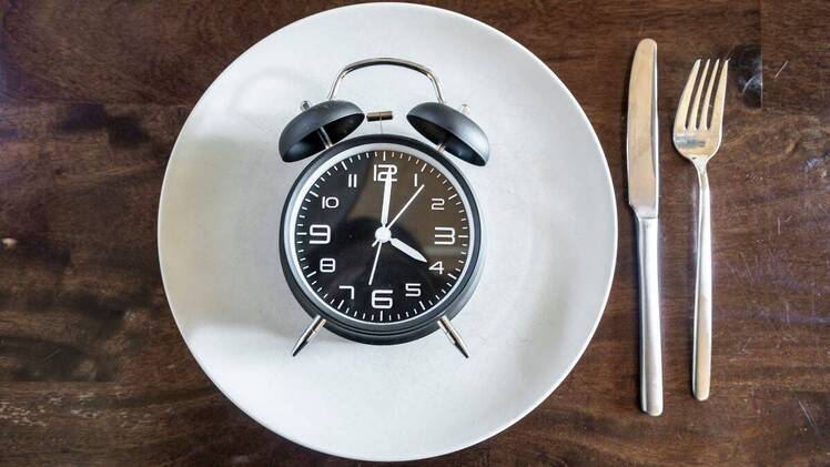 alarm clock on plate next to fork and knife on wooden table illustrating 43 fasting