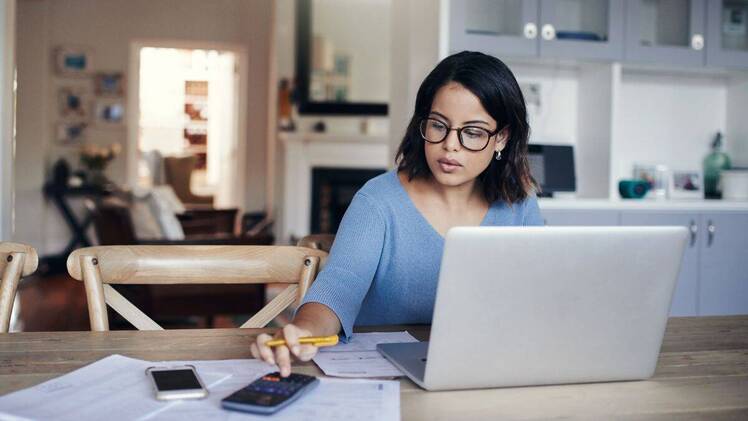 woman making calculations and working on laptop to balance student loans and retirement