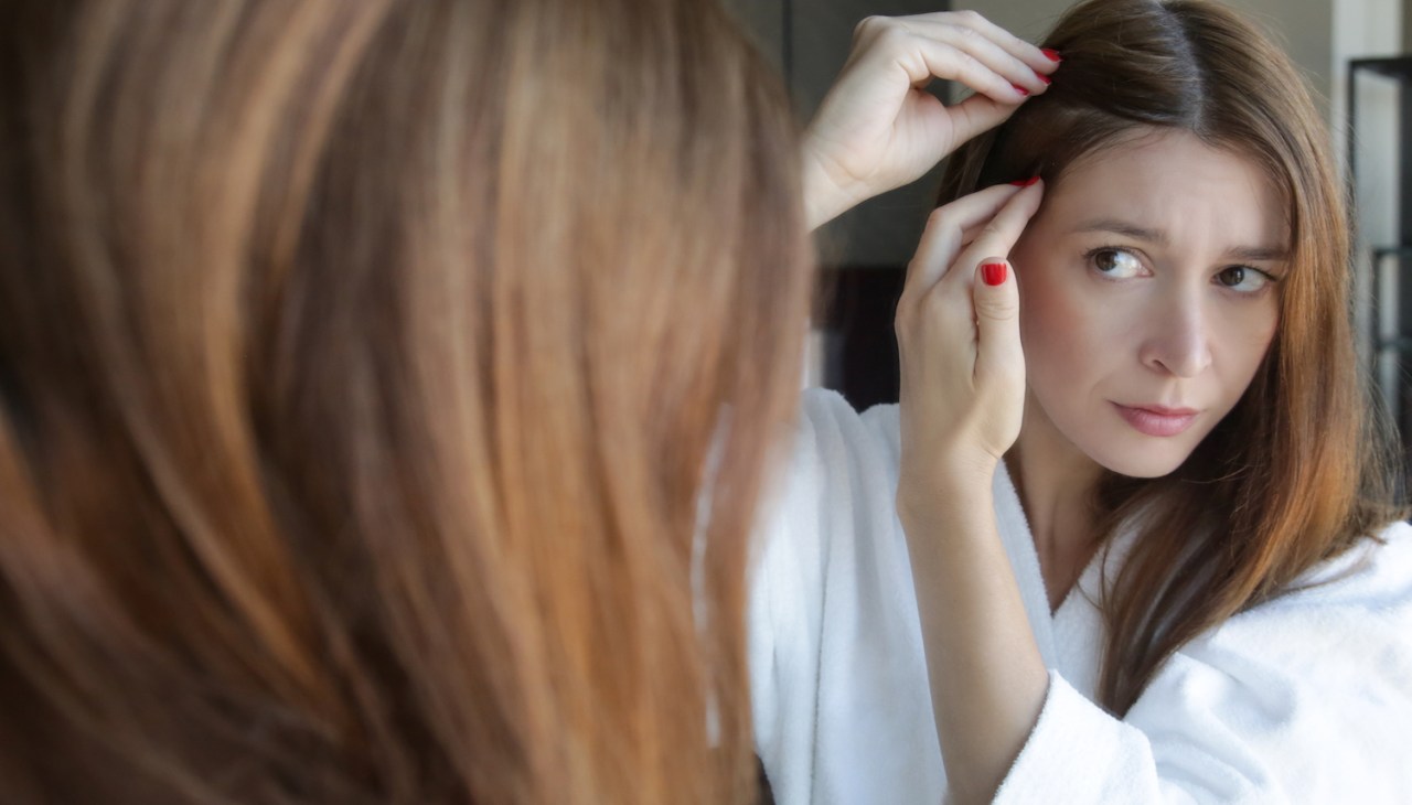 redhead woman examining hair near her scalp in a mirror