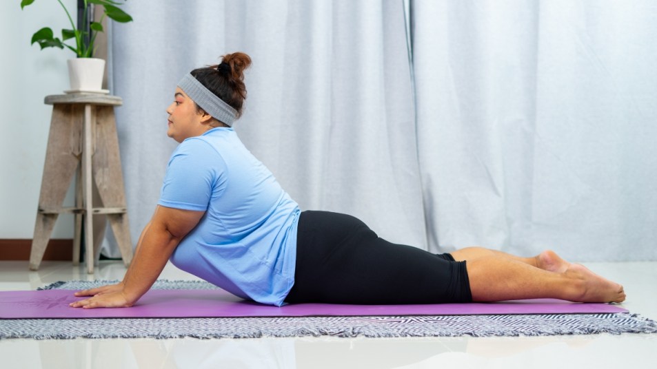 plus sized woman in blue shirt doing a cobra pose as part of a pilates workout