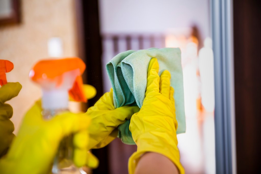 Woman in rubber gloves wipes the mirror in the room cleans after reading how to clean a mirror without windex