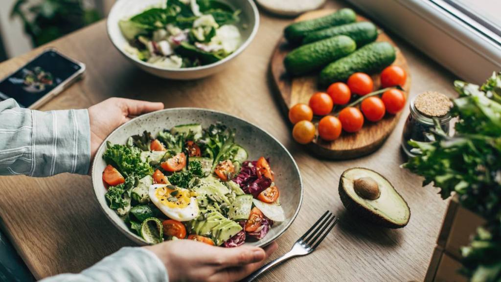 what to eat on ozempic: Woman mixing delicious superfood salad ingredients with wooden spoons in kitchen