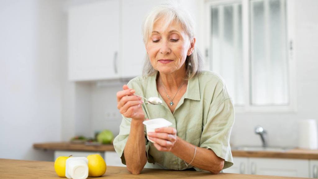Portrait of smiling retried woman enjoying yogurt as healthy snack in home kitchen