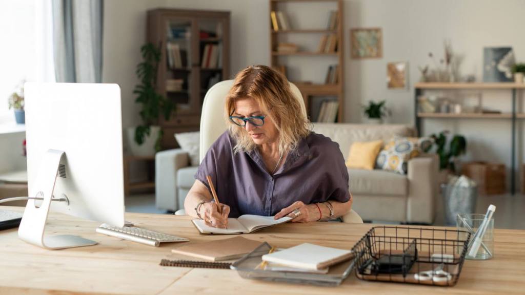 best state to work remotely: Busy mature female in eyeglasses and casualwear making notes or writing down points of working plan in front of computer monitor