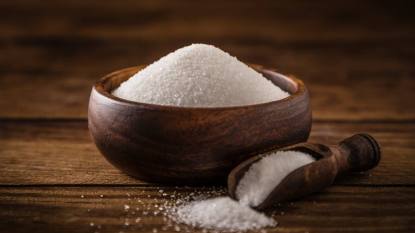 xylitol study: Front view of a wooden bowl full of white sugar beside a serving scoop against a rustic wooden table. Predominant color is brown