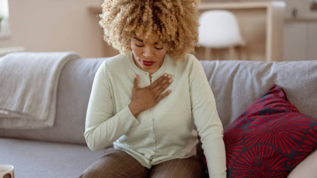 xylitol study: African American woman feeling sick and holding her chest in pain while sitting on the sofa in the living room