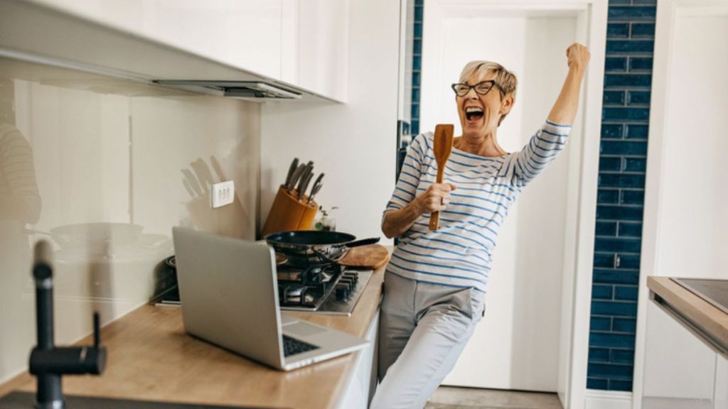 mature woman singing in her kitchen while holding a spatula to increase oxytocin levels