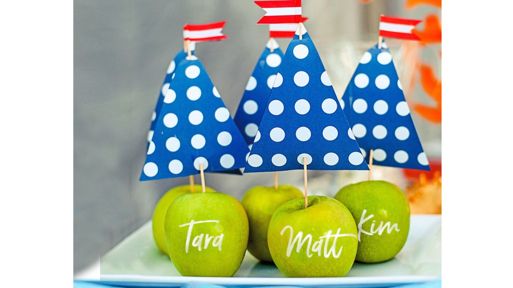 DIY beach decor: Blue polka dot paper sail picks staked into green apples adorned with dinner guests' names and displayed on a white platter