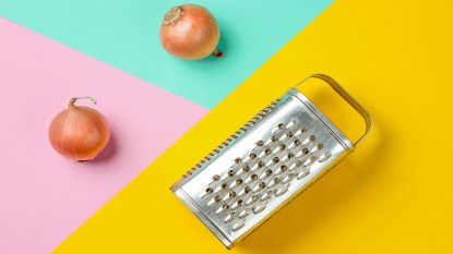 Box grater on a colorful background next to onions