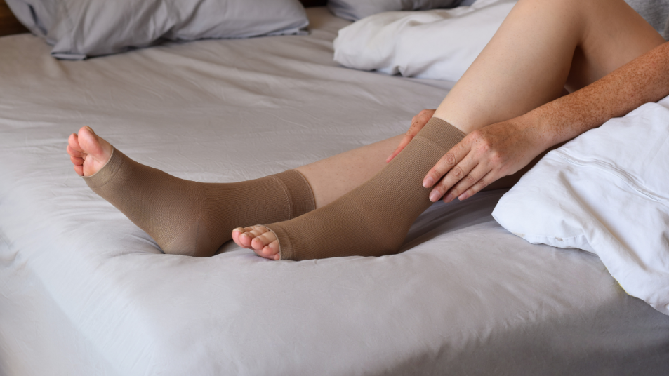 Woman sits on bed and puts on tan compression socks