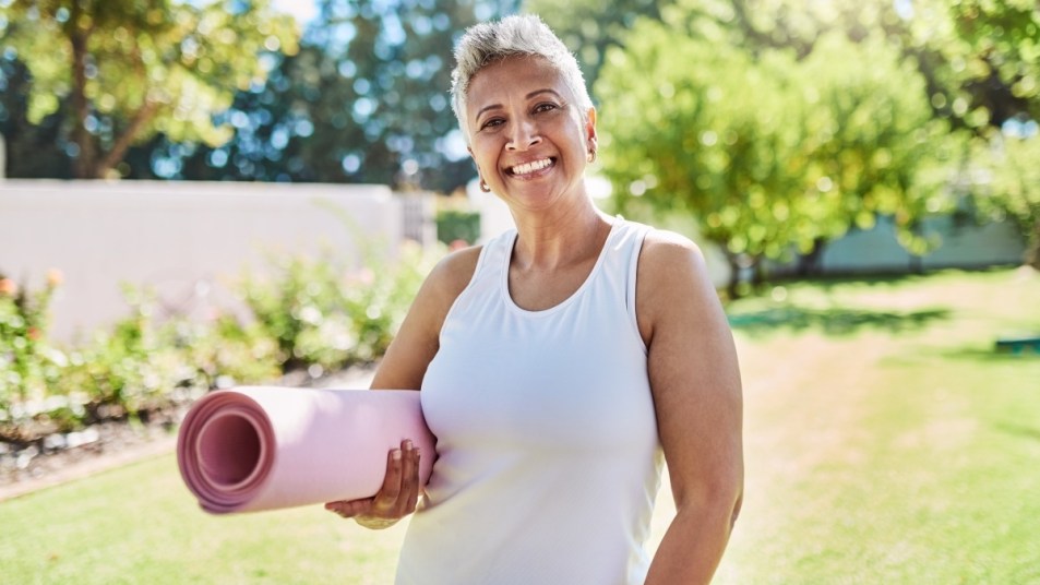 A mature woman holding a yoga mat outdoors after being explained the different types of yoga