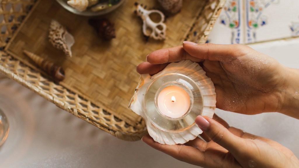 DIY beach decor: Female holding a scallop shell topped with a tea light candle above a wicker tray on a tabletop