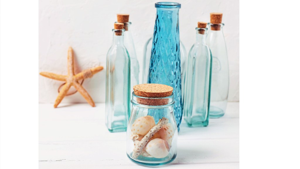 DIY beach decor: Decorative bottles, starfish, shells and shell-filled jar on white textured background