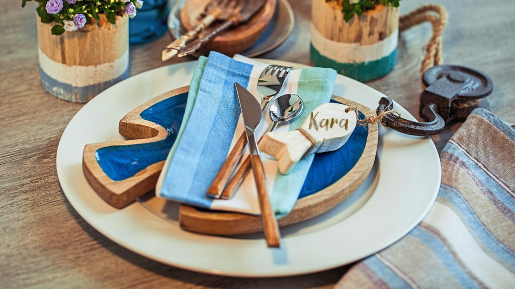 DIY beach decor: Beachy place setting consisting of a dinner plate topped with a fish-shaped salad plate, striped cloth napkin, cutlery and a name-adorned fish ornament on a dinner table