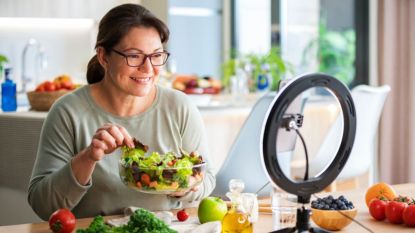 Mature woman who is a nutrition influencer over 50 filming herself cooking with ring light