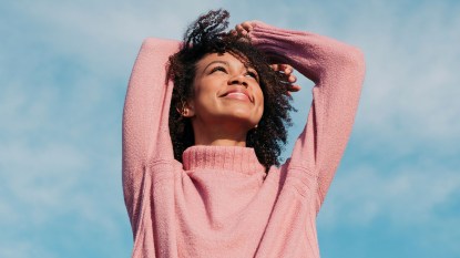Happy woman in pink sweater looking at bright blue sky