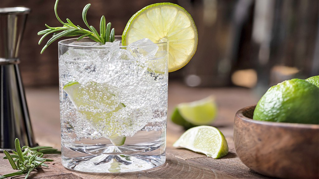 A gin and tonic drink garnished with rosemary and lime