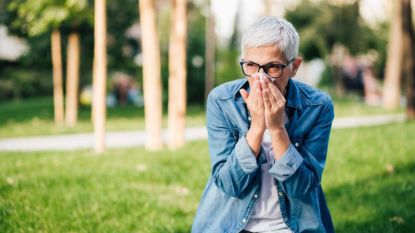 mature woman experiencing a summer cold outside blowing her nose